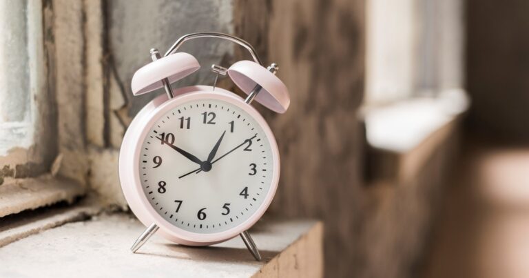 Reloj analógico siendo ajustado con un fondo de amanecer en una ciudad europea.